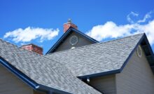 A close-up view of a house's gray shingle roof with a portion of the light beige siding visible.